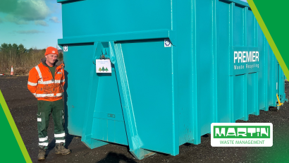 A premier waste worker stands beside a large blue skip used to collect unwanted Christmas Trees to raise funds for St Cuthberts Hospice.