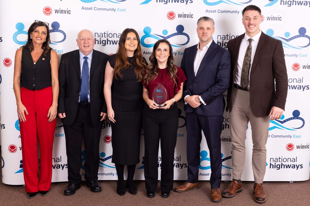 Group of 6 people standing in front of a background featuring the National Highways and the ACE Community Award logo