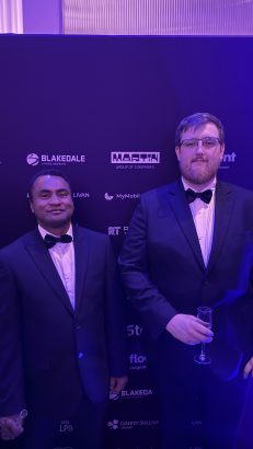 On the left Jikoto Nowa and on the right Andrew Hobson. The pair pose in front of a branded backdrop at the Heroes Awards in London. The backdrop features sponsor logos including the Martin Group of Companies.